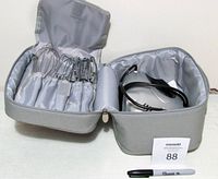 Photo of open gray zippered storage bag showing multiple stainless steel attachments including whisks and beaters