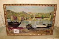 Full view of the framed oil painting showing boats on riverbank with town and mountains in background.