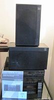 Photo of stacked stereo components with two speakers on top and instruction manual in front.