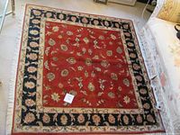 Overall view of square Persian rug on carpeted floor.
