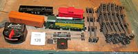Vintage American Flyer train set components including locomotive, caboose, box cars, transformer, tracks, decoupler, and track terminal laid out on a surface.