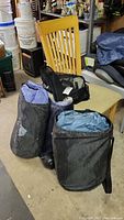 Three black carrying bags for air mattresses, two with visible Ozark Trail logo, placed next to a wooden chair in a basement.