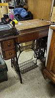 Side view of antique Singer treadle sewing machine showing wooden cabinet, drawers, and iron base with treadle pedal and SINGER branding.