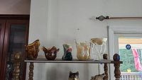 Wide shot of all glass and ceramic vases and bowls arranged on a narrow table showing their relative sizes and designs.