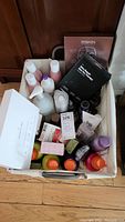 Top view photo of white basket filled with various beauty products including bottles, tubes, facial mask packets, and creams.