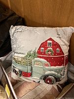 Decorative pillow with holiday theme showing vintage green truck and red barn with wreath, snowy scene