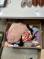 Box containing folded women's clothing in various colors and patterns including socks and pants.