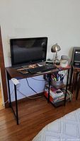 Desk with woodgrain surface, metal frame legs, two side shelves loaded with office supplies and a computer keyboard and monitor on top.