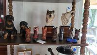 Full view of the upper shelf showing two Rottweiler statues, seven ceramic cowboy boots, and two mounted wolf head statues with wood bases.