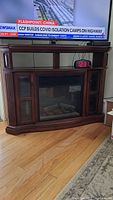 Front view of dark wood electric fireplace with digital clock on center shelf and TV above.