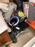 Photo of Pro Form exercise bench surrounded by stored household items and sports equipment including tennis rackets, exercise pad, and waist exerciser belt.
