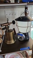 Harley Davidson lantern and vintage brass blow torch shown side by side on a shelf.