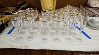 Full set of 21 full lead crystal stemware glasses arranged in three rows on a white cloth showing gold rims on each glass
