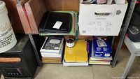 Wide view showing assortment of office supplies including Pendaflex folders in multiple colors, black planner, notebooks, yellow file, and boxes of paper.