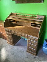 Front view of wooden roll top desk showing drawers, roll top cover partially open, and rear shelf with spindles.