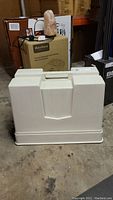Closed beige hard plastic carrying case for sewing machine.