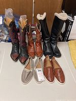 Overview photo showing all six pairs including two pairs of cowgirl boots, two pairs of winter boots, and two pairs of casual slip-on shoes arranged on a table.