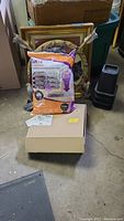 Lot contents including gold-tone framed owl picture, vacuum bags, stacked other items in background.