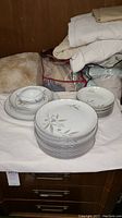 Stack of white china plates and bowls with floral pattern and beige-green leaves, various sizes.