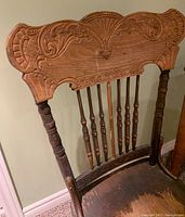 Close up of the hand carved detailing on the press back of the antique wooden chair showing ornate scroll and shell motifs.