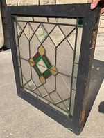 Front view of stained glass window showing geometric pattern of glasses in purple, amber, green colors and textured glass with black painted wooden frame that shows chipping.