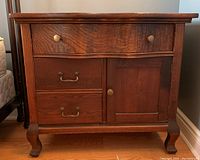 Front view of antique washstand showing serpentine front, wood grain, two drawers with brass handles, and cabinet door.