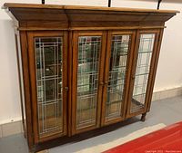 Front view of the antique wood display cabinet showing four leaded glass doors and mirrored back inside.