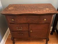 Front face of antique wood washstand showing tigerwood grain, serpentine profile top, and original metal pulls.