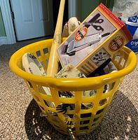 Yellow plastic laundry basket filled with a boxed grooming set, baseball bat, and textile items visible inside.