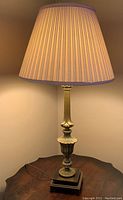 Vintage brass table lamp illuminated, showing beige pleated fabric shade and brass body on wooden base
