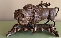 Side view of vintage bronze buffalo statue on ornate base, showing detailed texture of fur and curved horns.