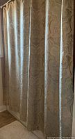 Shimmering fabric shower curtain with paisley pattern hung on rod, showing detailed design and colors in natural light.