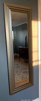 Full view of the full length rectangular wall mount mirror with silver brushed metal frame hung vertically on a wall, showing clear reflection.