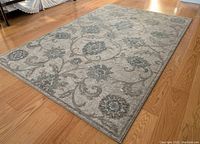 Area rug laid flat on hardwood floor showing the full pattern with beige, grey, and cornflower blue floral design.