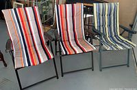 Three striped fabric lawn chairs side by side with metal frames and armrests, folding design.