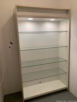 Full front view of the wood display cabinet showing four glass shelves and interior lighting with power cord on side.