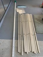 Photo showing long double slotted metal standards in beige and multiple beige slotted shelf brackets arranged on the floor.