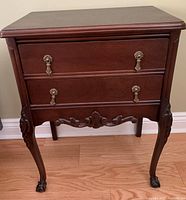 Front view of one solid wood antique side table showing two drawers with metal pulls, carved cabriole legs and claw feet.