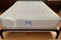 Top view of queen size white Sealy mattress on bed frame showing quilted pattern and label.