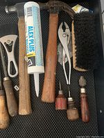 Tools arranged in drawer showing hammer, caulking tube, pliers, wire brush, and small screwdrivers with wooden handles.