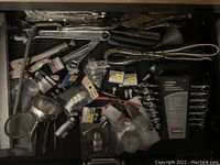 Variety of hand tools spread in a drawer including adjustable wrenches, pliers, driver bits, sockets, locking pliers, and wrenches with some still in packaging.