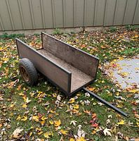 Full side view of a wood and metal trailer with two wheels on grass covered with autumn leaves