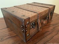 Angle showing side and top of brown faux leather vintage style storage box with embossed patterns, metal rivets, clasps, and handle.