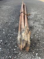 Two long wooden poles with metal pointed fork prongs laid on asphalt surface, bound with a leather strap.