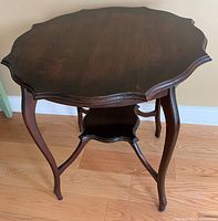 Photo showing top and legs of vintage dark wood accent table with scalloped edged top and lower shelf