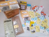 Top view of the entire lot showing multiple small parts kits and scenic detail packages scattered on table with a brown cardboard box marked 'HO Details'. Includes boxed kits and loose parts in plastic bags.