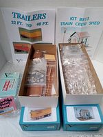Two open boxes showing unassembled plastic model parts for a train reefer trailer kit and a train crew shed kit with booklet instructions.