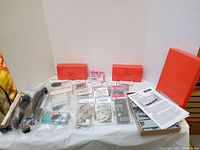 Lot of various HO scale vintage train model kits and detail parts arranged on a white cloth background. Includes boxes, plastic bags with parts, instructions and decals visible.
