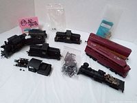 Several vintage HO scale train car shells and loose parts, including black and burgundy pieces and bags with details.