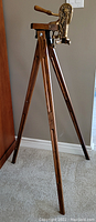 Full front view of wooden tripod with mounted vintage brass wine bottle opener
